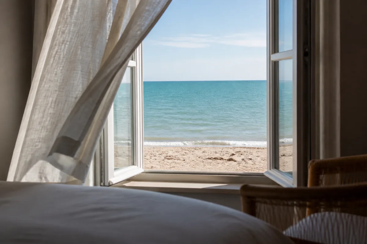 Fenêtre d’une chambre d’hôtel ouverte sur une plage et l’horizon marin